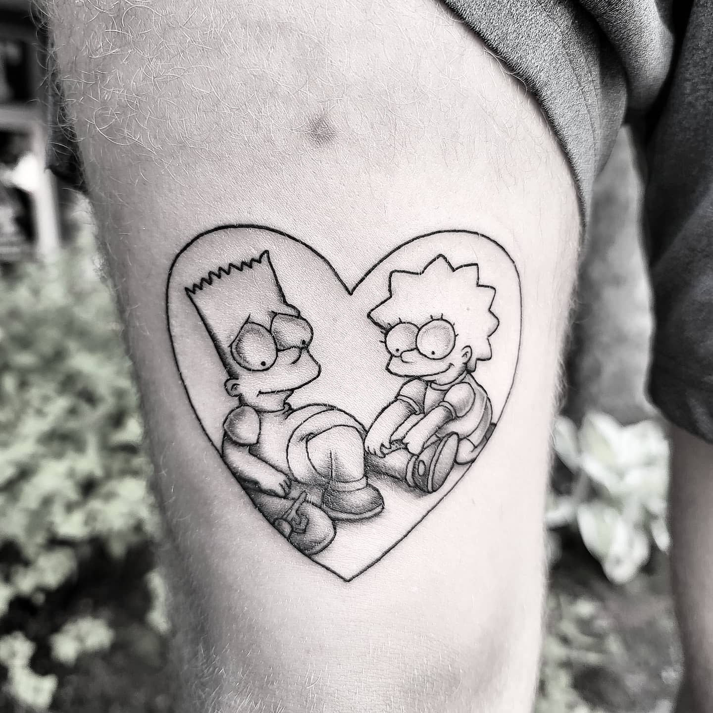 Tattoo of cartoon siblings Bart and Lisa Simpson sitting inside a heart shape on a leg